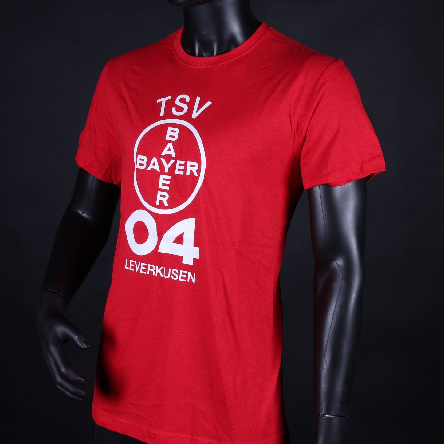 Rotes Kinder-T-Shirt mit großem weißen Vereinslogo „TSV Bayer 04 Leverkusen“ auf der Vorderseite, präsentiert an einer Schaufensterpuppe vor schwarzem Hintergrund.