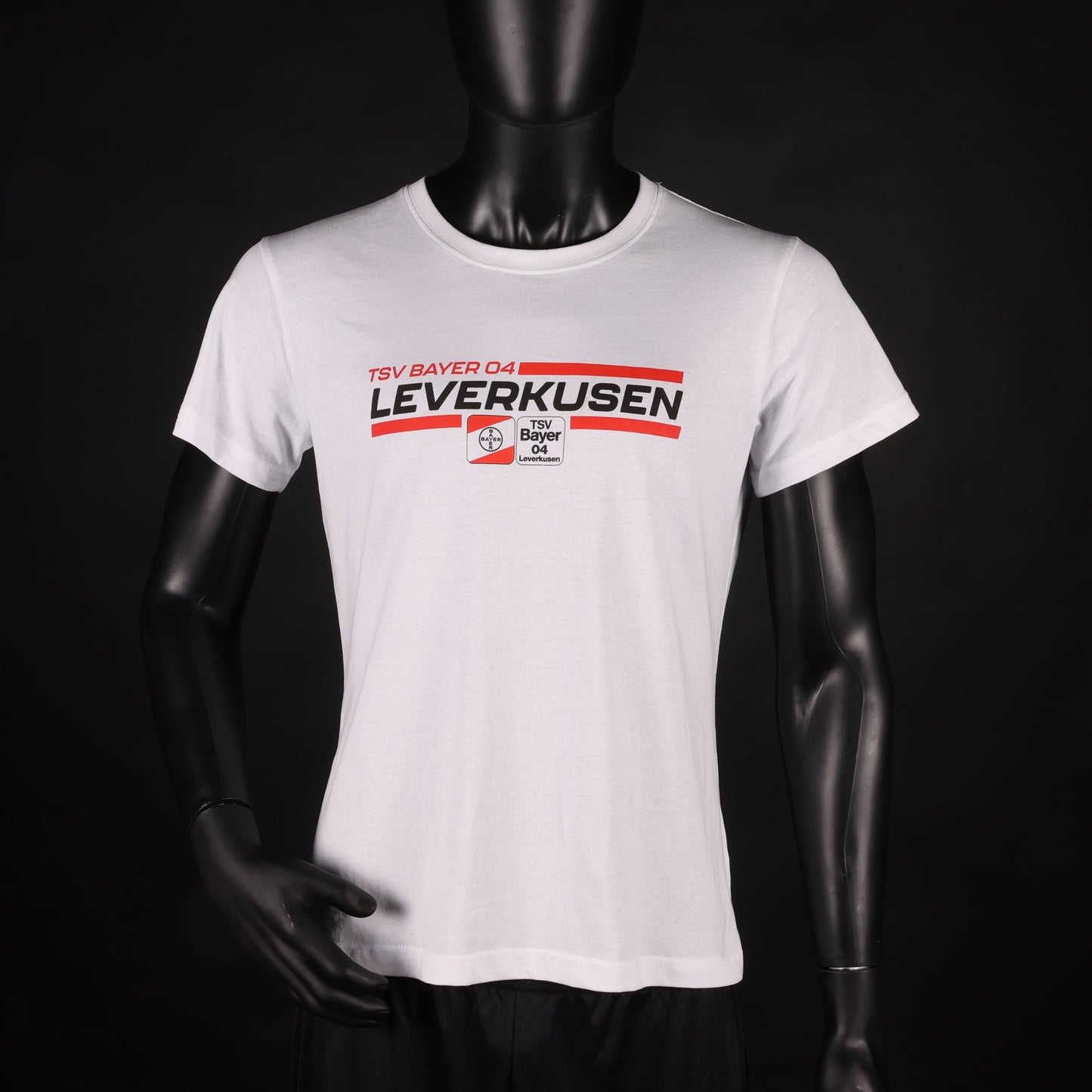 Weißes T-Shirt mit rotem und schwarzem „TSV Bayer 04 Leverkusen“-Schriftzug und Vereinslogo in der Mitte, präsentiert an einer Schaufensterpuppe vor schwarzem Hintergrund.