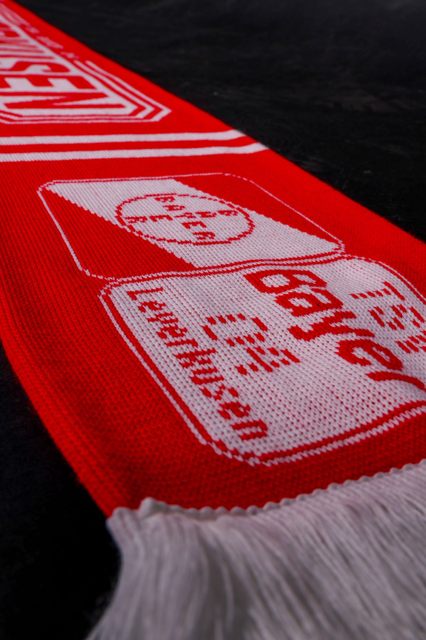 Detailansicht des rot-weißen TSV-Bayer-04-Leverkusen-Fanschals mit Vereinslogo und Schriftzug ‚TSV Bayer 04 Leverkusen‘, am unteren Rand mit weißen Fransen.