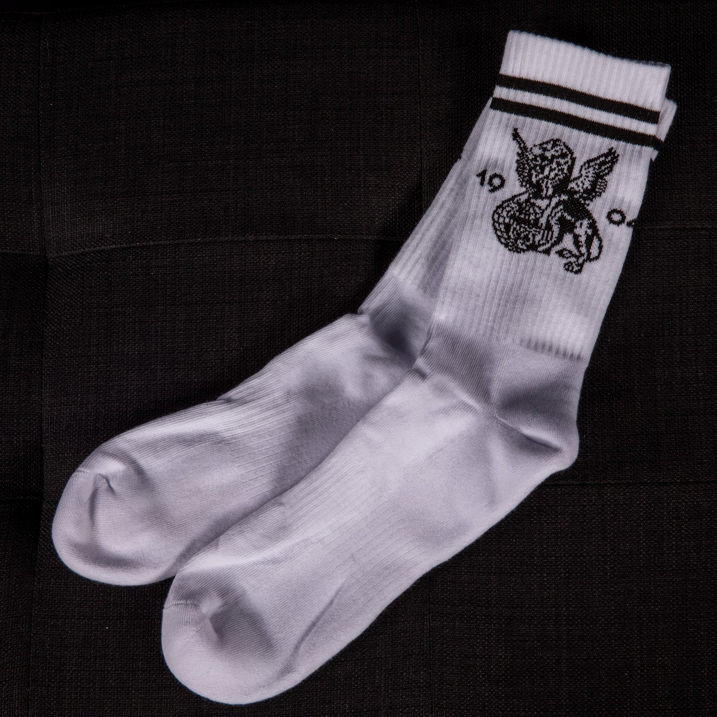 Komplett ausgepackte weiße Sportsocken mit schwarzen Streifen und detailreichem geflügeltem Löwenmotiv – flach liegend dargestellt.