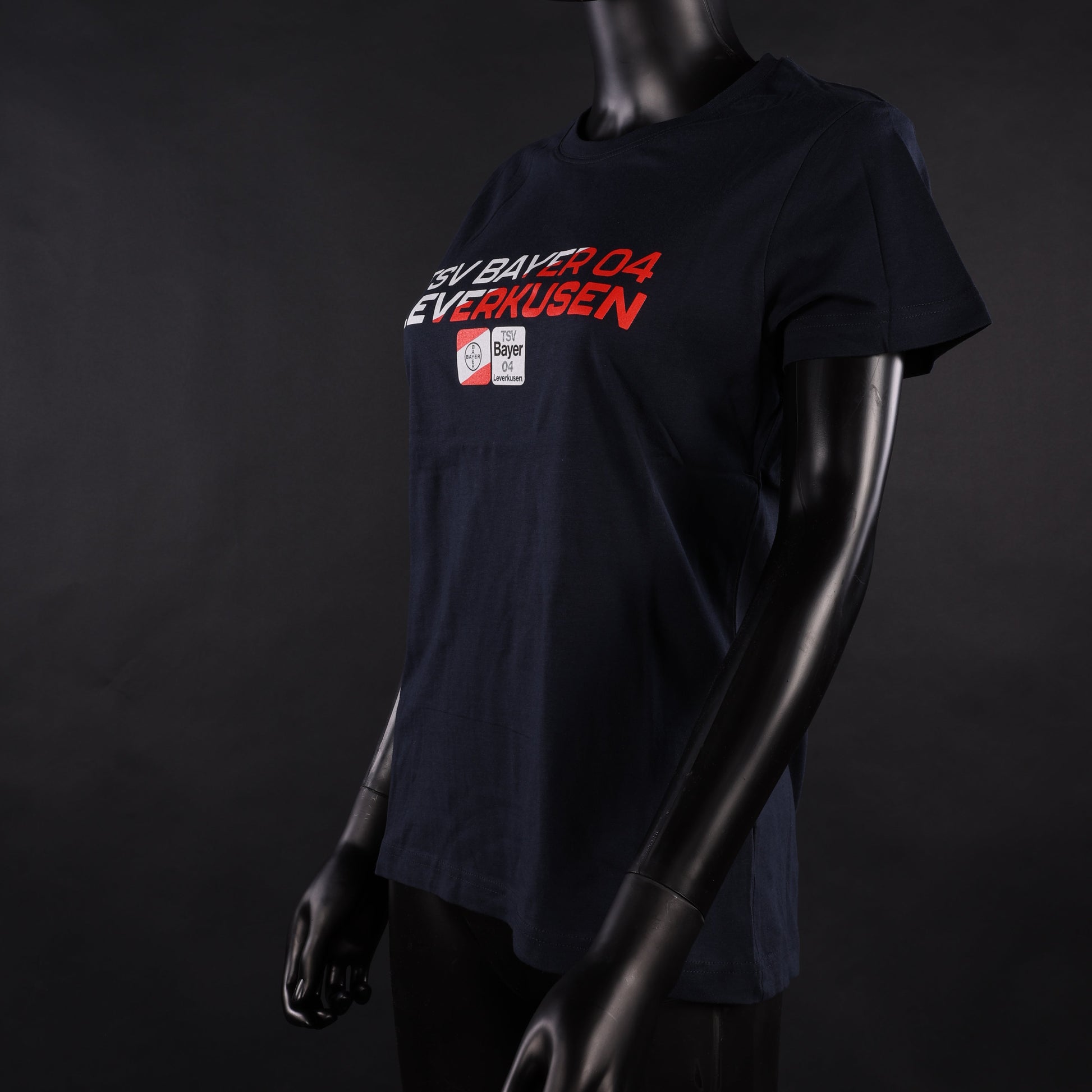 Dunkelblaues Damen-T-Shirt mit rotem und weißem „TSV Bayer 04 Leverkusen“-Schriftzug und Vereinslogo, schräg von vorne fotografiert an einer weiblichen Schaufensterpuppe vor schwarzem Hintergrund.