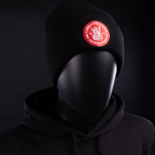 Schwarze Strickmütze mit rotem Patch des TSV Bayer 04 Leverkusen, getragen von einer Schaufensterpuppe mit passendem Hoodie.