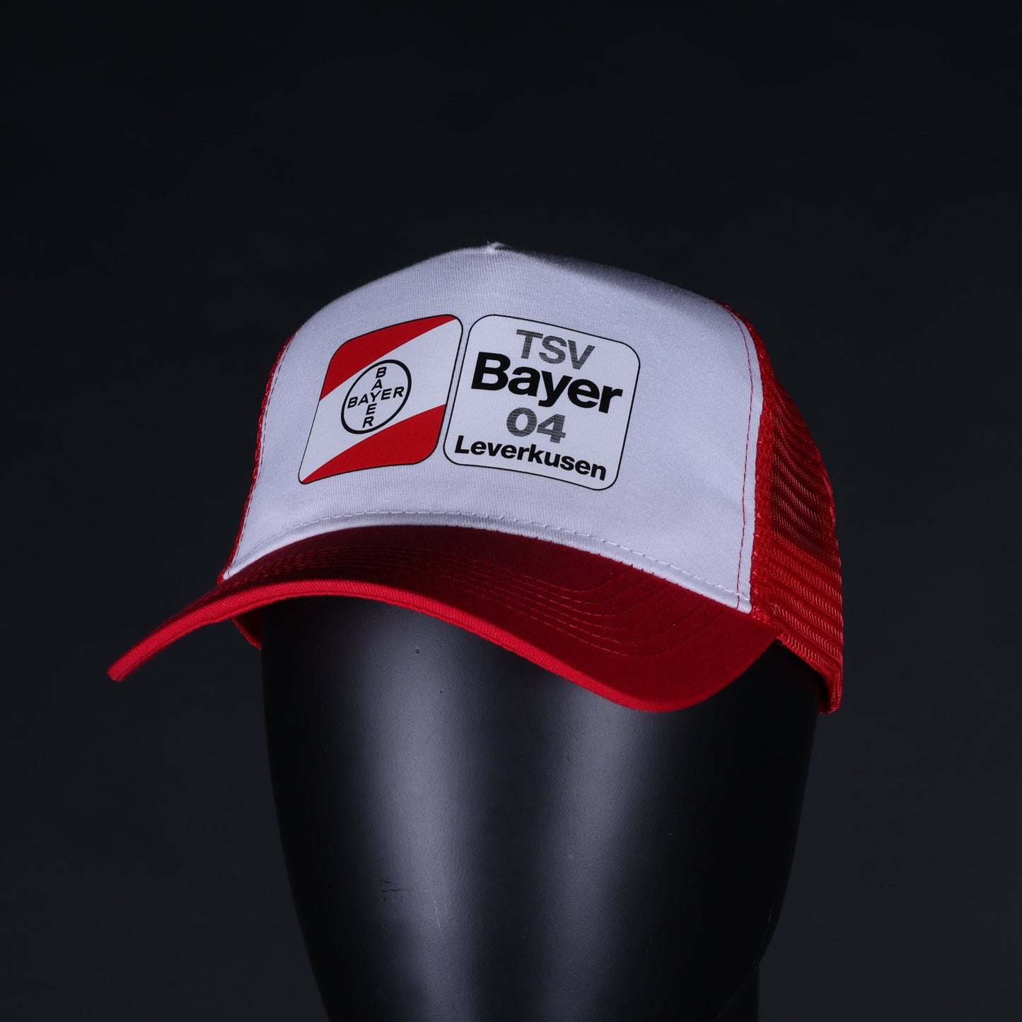 Rote und weiße Trucker-Cap mit Netzrückseite und gebogenem Schirm, getragen auf einem Schaufensterkopf; vorne das Logo des TSV Bayer 04 Leverkusen in Schwarz, Weiß und Rot.