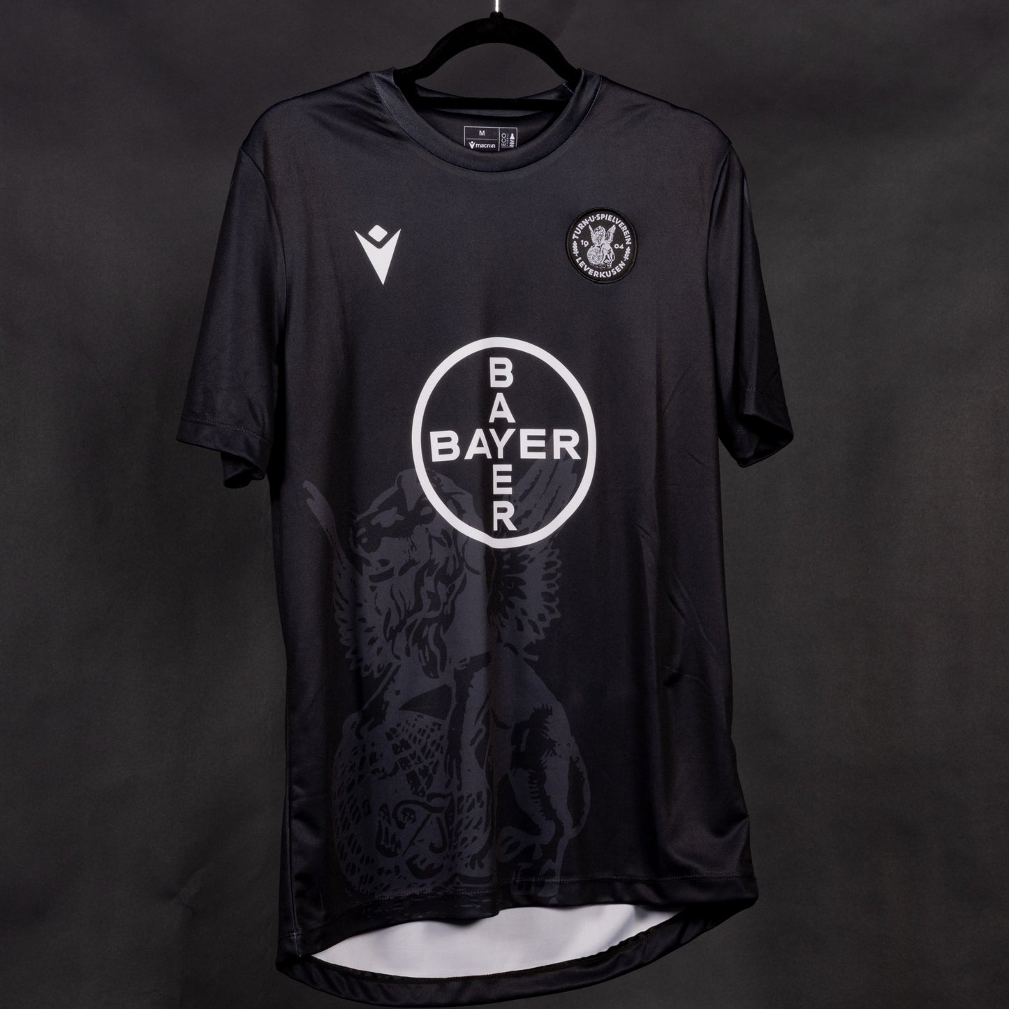 Schwarzes Sondertrikot des TSV Bayer 04 Leverkusen mit weißem Bayer-Kreissymbol auf der Brust, dezentem Löwenmotiv im unteren Bereich und Vereinslogo auf der linken Brustseite.