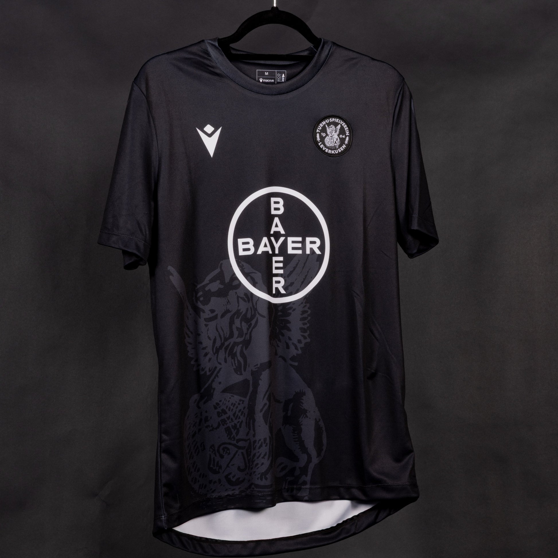 Schwarzes Sondertrikot des TSV Bayer 04 Leverkusen mit weißem Bayer-Kreissymbol auf der Brust, dezentem Löwenmotiv im unteren Bereich und Vereinslogo auf der linken Brustseite.