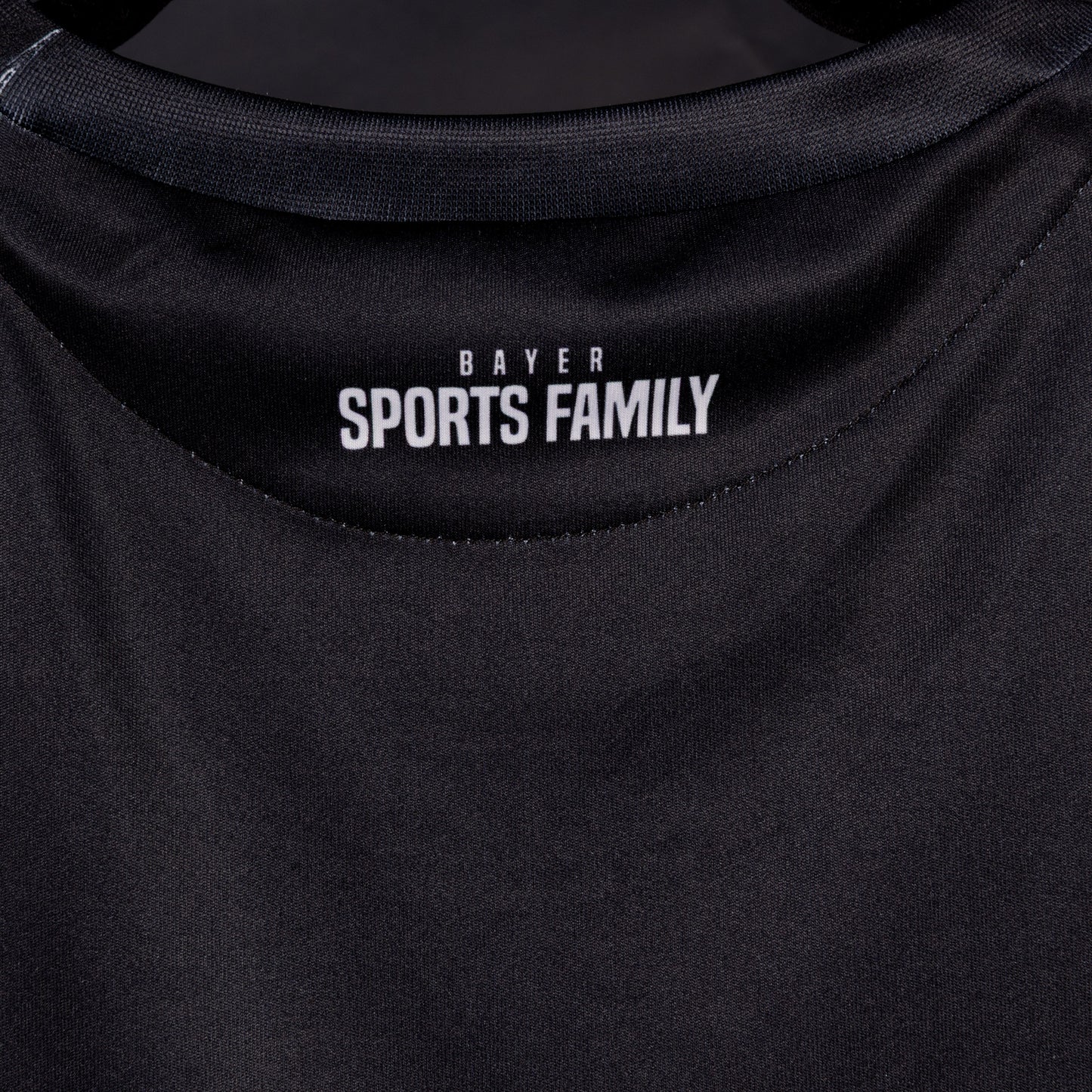 Nahaufnahme der Rückseite des Sondertrikots von TSV Bayer 04 Leverkusen mit weißem Nackenprint ‚Bayer Sports Family‘ unter dem Kragen.