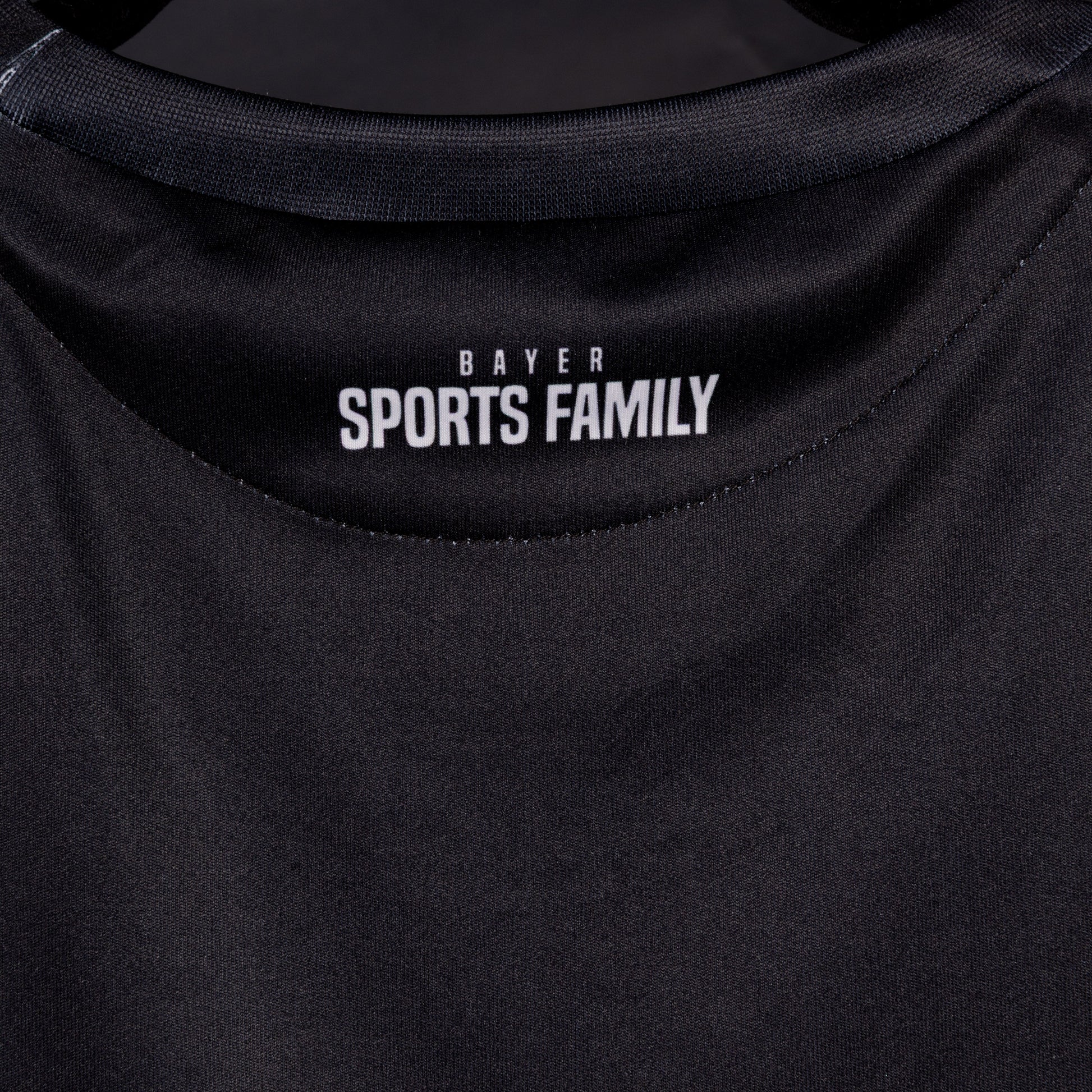 Nahaufnahme der Rückseite des Sondertrikots von TSV Bayer 04 Leverkusen mit weißem Nackenprint ‚Bayer Sports Family‘ unter dem Kragen.