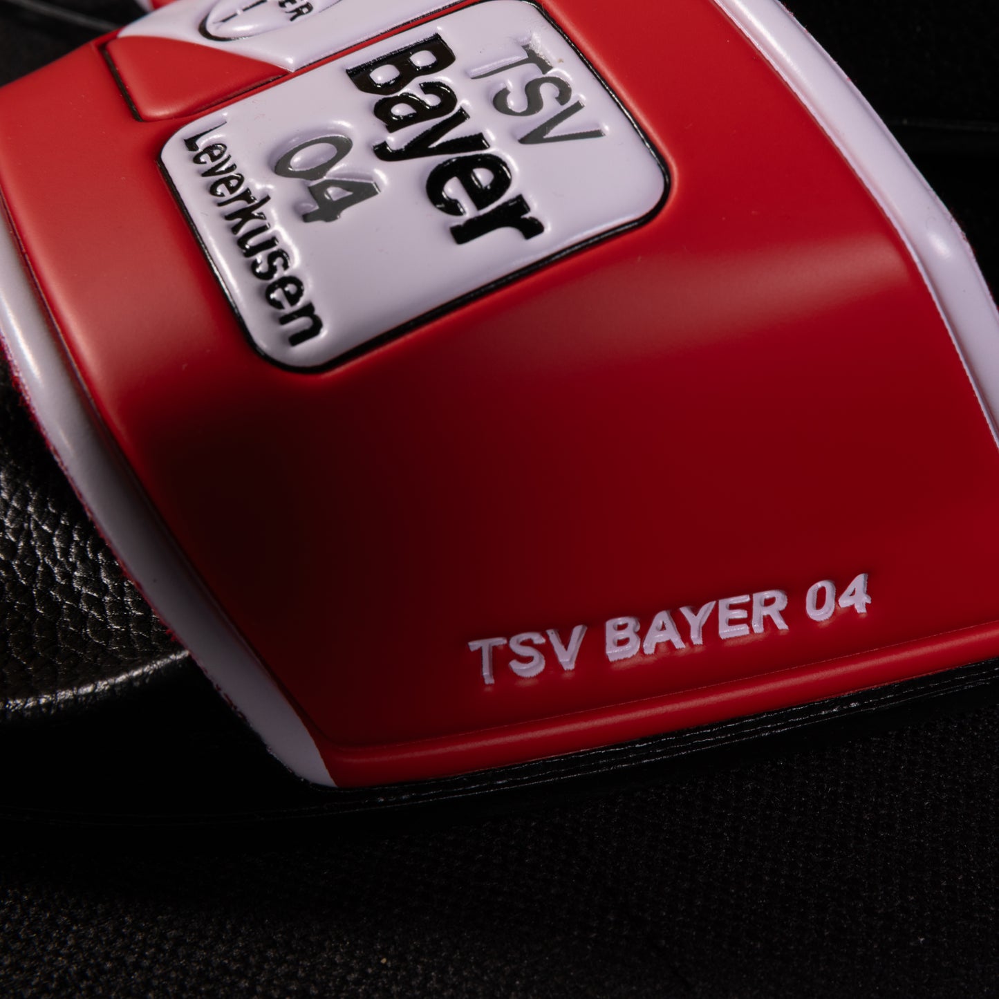 Nahaufnahme der roten TSV Bayer 04 Leverkusen Badelatsche mit geprägtem Schriftzug „TSV BAYER 04“ auf dem seitlichen Riemen.