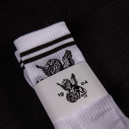 Weiße Sportsocken mit schwarzen Streifen und Löwenmotiv, in Verpackung mit geflügeltem Löwenlogo und der Jahreszahl 1904 – Vorderansicht.